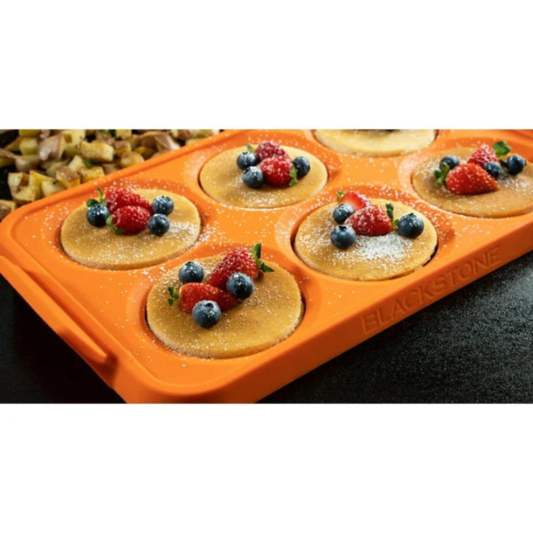 Orange silicone pancake mold with mini pancakes topped with berries on a white background