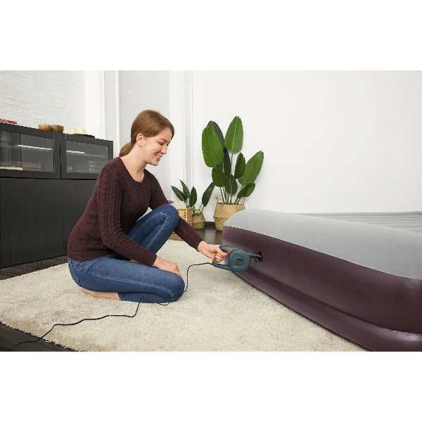 Woman inflating an air mattress in a room with plants and furniture.
