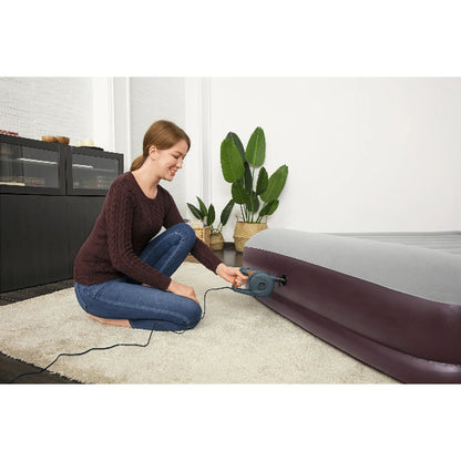 Woman inflating an air mattress in a room with plants and furniture.