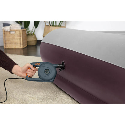 Person inflating a mattress with an electric pump in a room setting.
